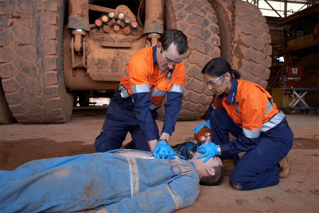 Two industrial employees performing first aid on a colleague